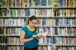 Student reading book in library in front of shelves